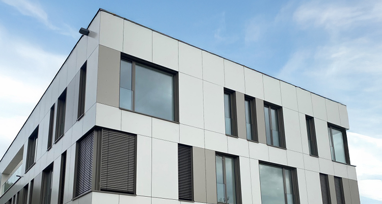 Moderne Gebäudefassade mit weiß-grauen ALPOLIC® Aluminium-Verbundplatten und großflächigen Fenstern unter blauem Himmel Kachel