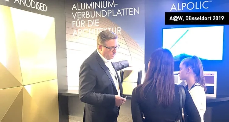 Blick auf den Messestand von ALPOLIC, wo sich gerade ein Vertriebsmitarbeiter mit zwei Interessenten unterhält 