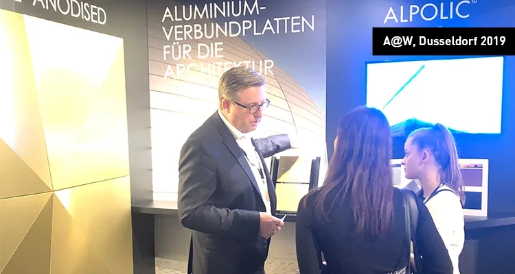 Architect@Work Düsseldorf Vue du stand ALPOLIC™, où un représentant commercial s'entretient avec deux personnes intéressées.